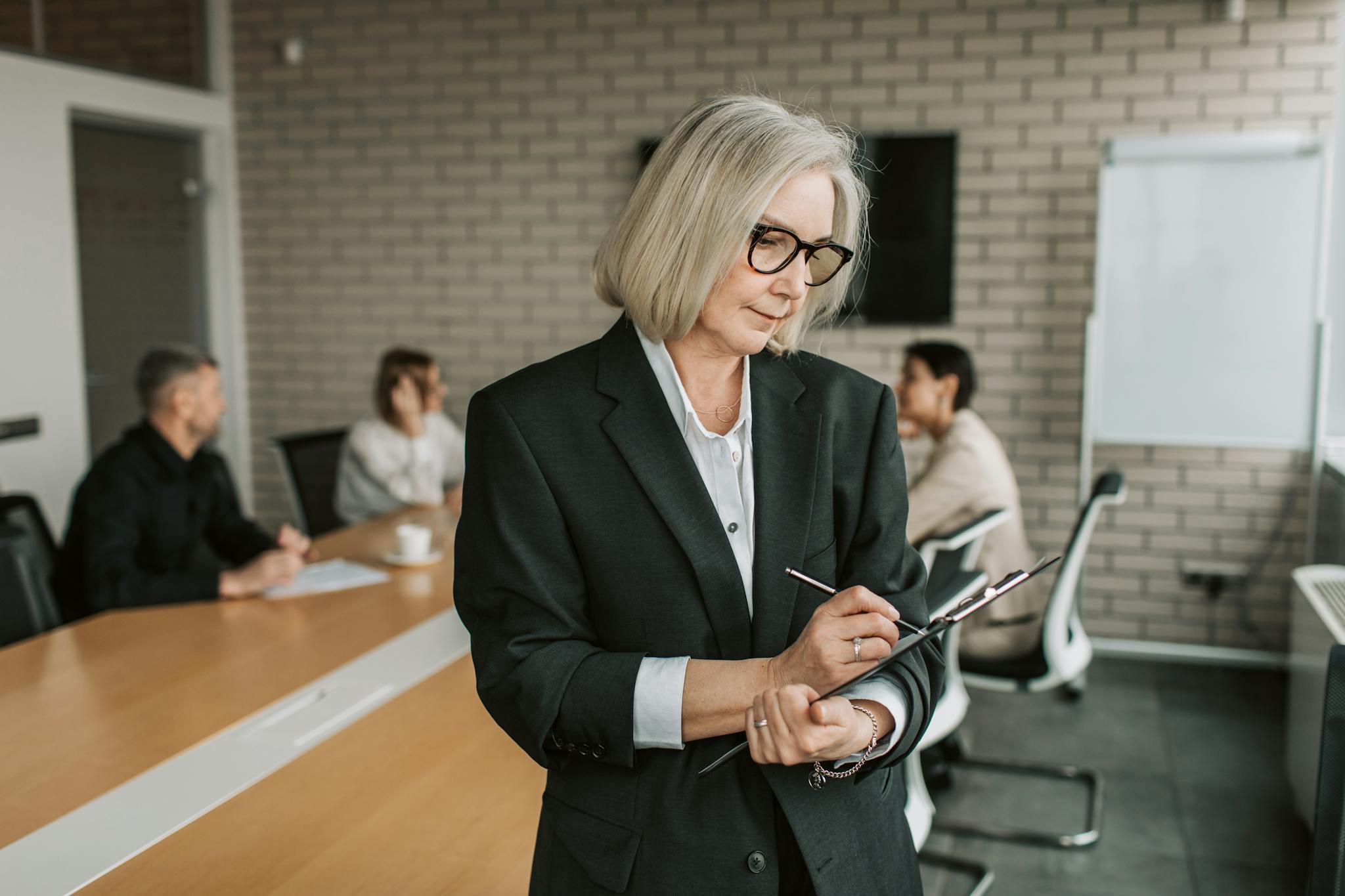 Senior businesswoman in black blazer overseeing a team meeting in a modern corporate office.