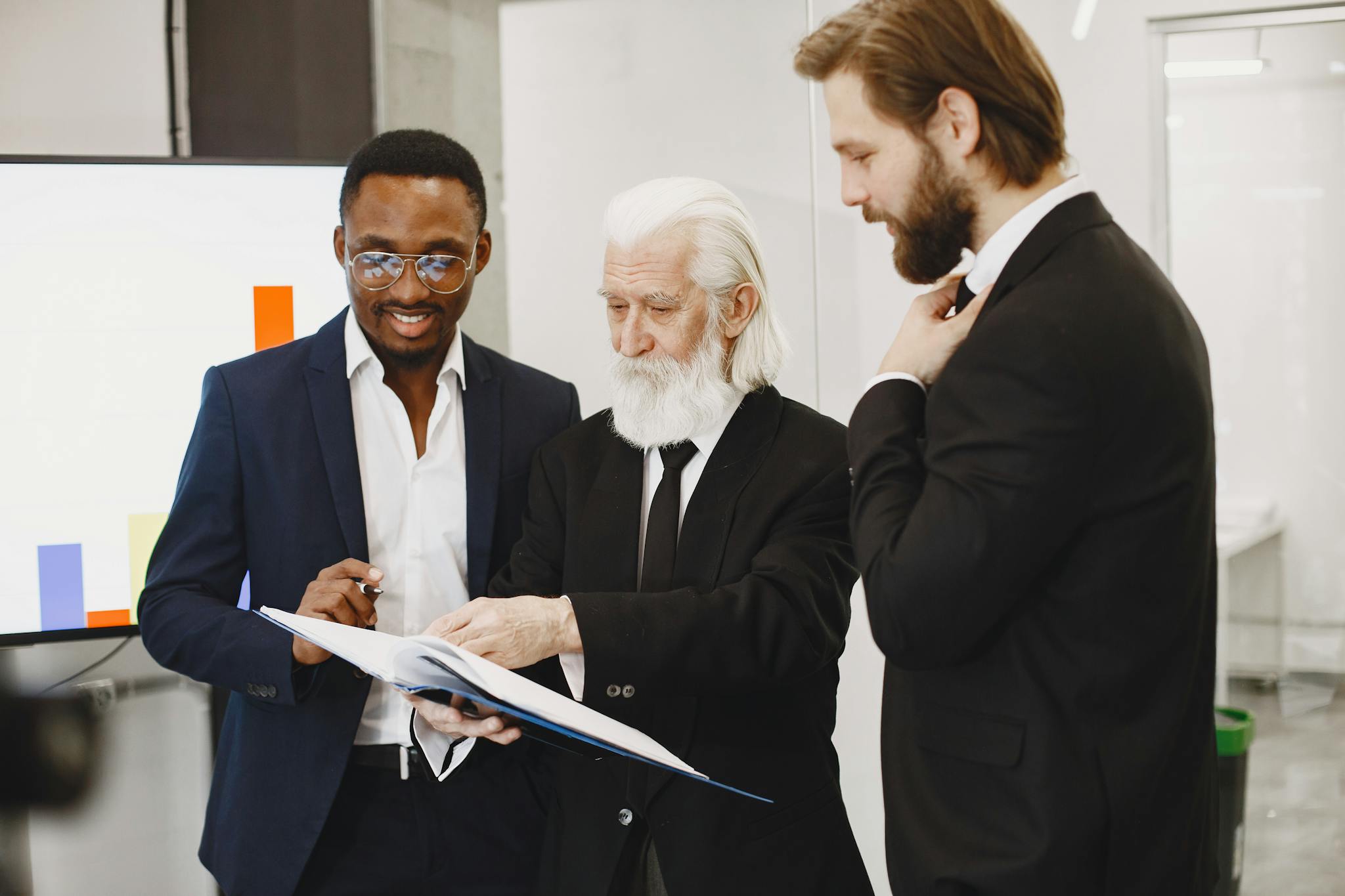 Three businessmen in suits reviewing documents in a modern office setting.